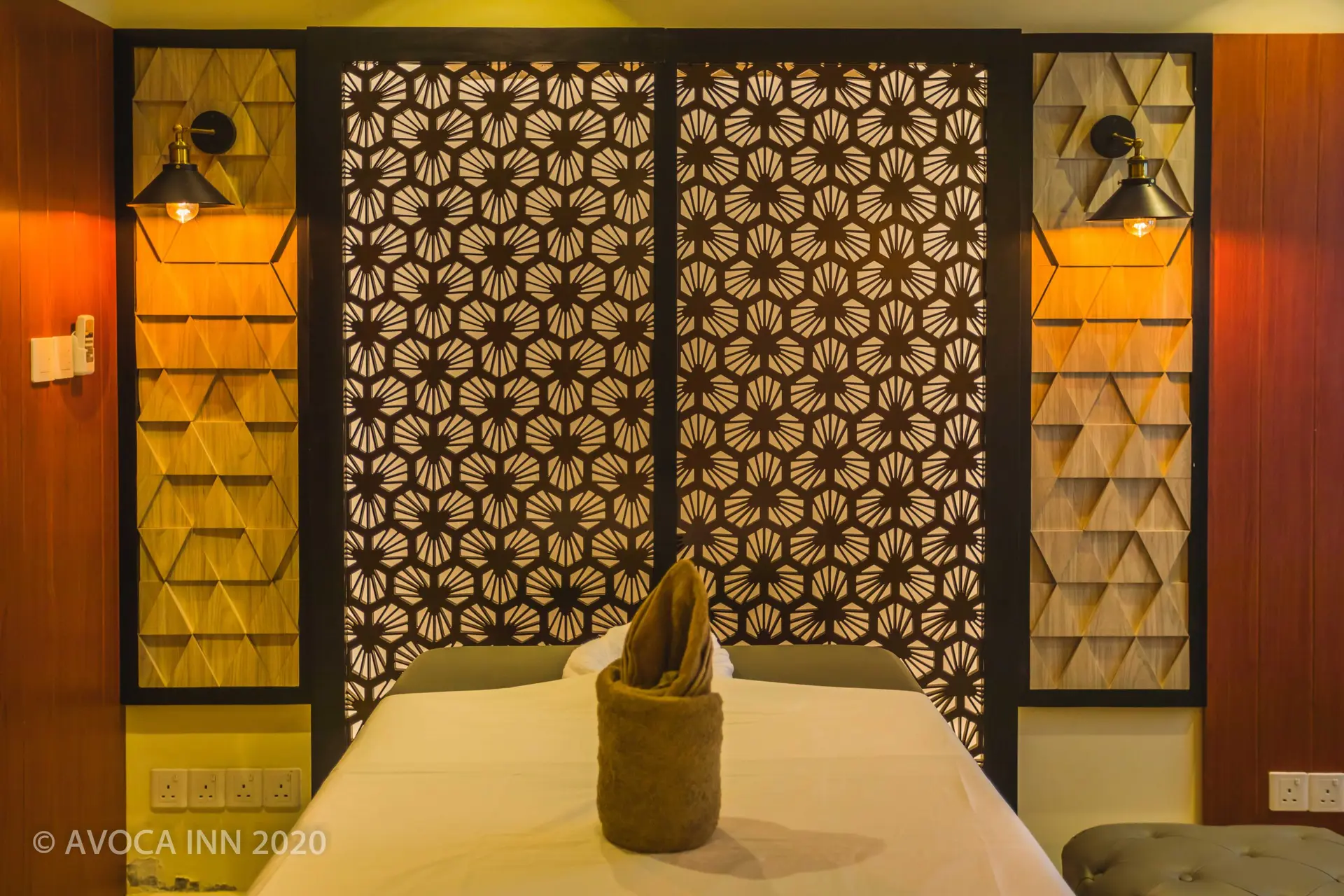 A luxurious hotel room features a serene bed with geometric patterned headboard and warm lighting.