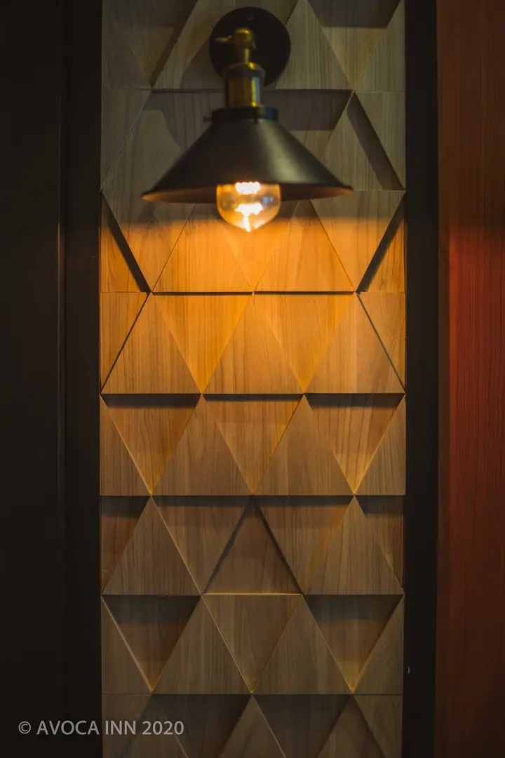 Avoca Inns geometric wood wall is illuminated by a stylish lamp, creating a warm and inviting room ambiance.